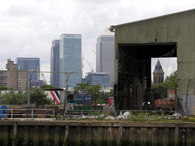 Photo of sheds in disrepair with Canary Wharf in the background